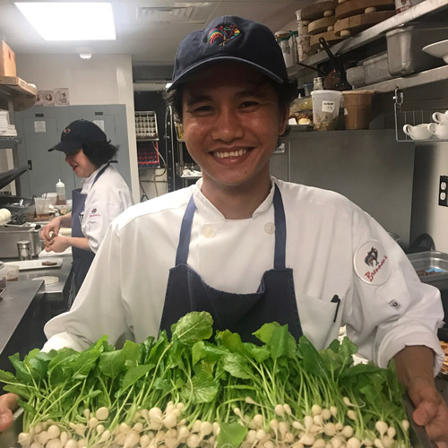 Member of Kitchen staff holding tray of fresh veggies